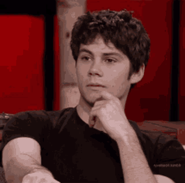 a young man is sitting down with his hand on his chin .