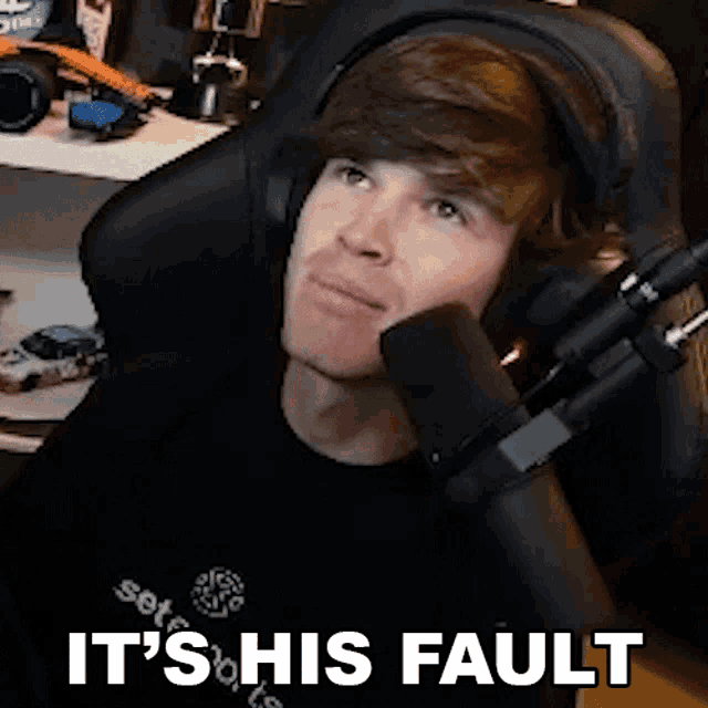 a man wearing headphones is sitting in front of a microphone and saying it 's his fault