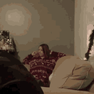 a woman is sitting on a couch in a living room wearing a sweater .