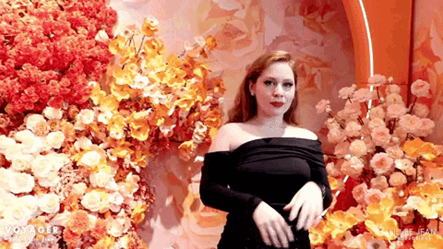 a woman in a black dress is standing in front of a wall of flowers with voyager written on it