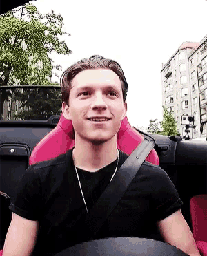 a young man in a black shirt is sitting in a car with a pink seat