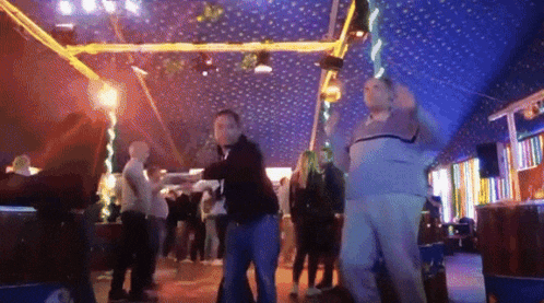 a group of people are dancing in a dark room with a blue ceiling