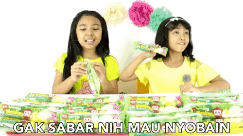 two young girls are sitting at a table with candy bars and the words " gak sabar nih mau nyobain "
