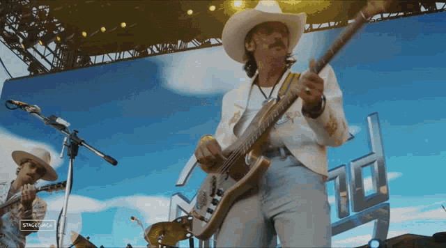 a man in a cowboy hat is playing a guitar in front of a sign that says stagewalk