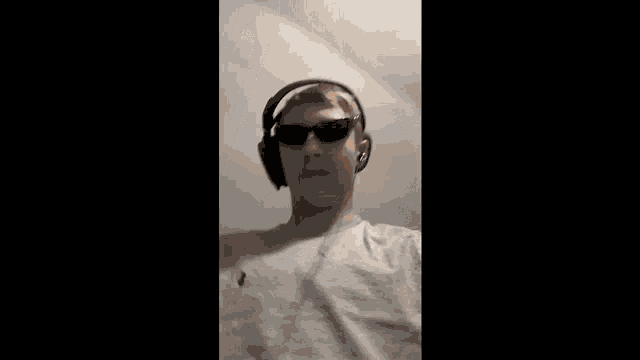 a young man wearing headphones and sunglasses is making a funny face .