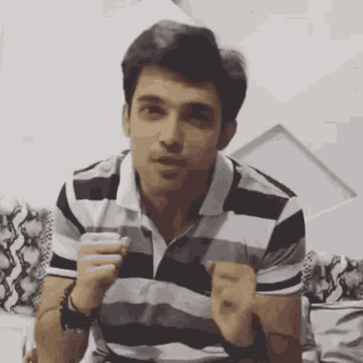 a man in a striped shirt is sitting on a couch and making a face .