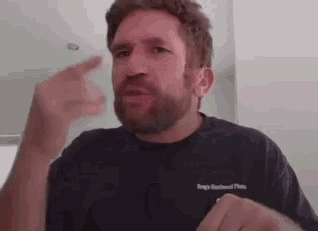 a man with a beard is wearing a black t-shirt and pointing at something .