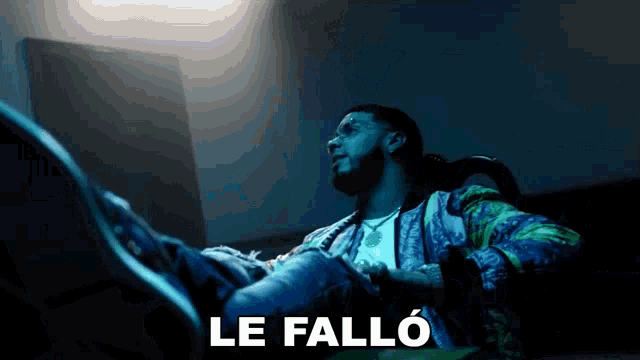 a man in a colorful jacket sits in a dark room with the words le fallo written above him