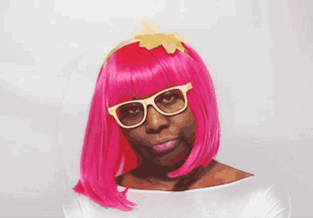 a woman wearing a pink wig and sunglasses looks at the camera