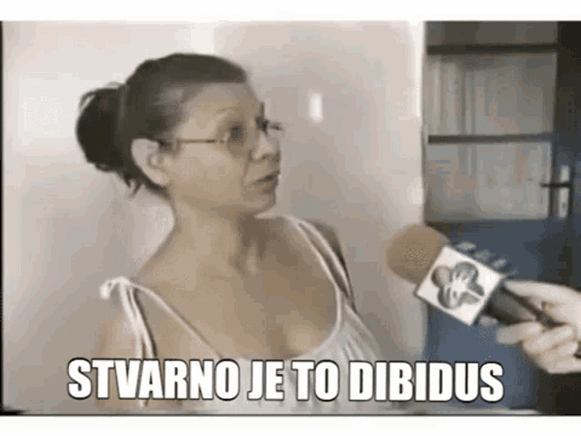 a woman with glasses is talking into a microphone with the words stvano je to dibidos written on it .