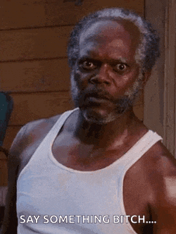 an older man with a beard is wearing a white tank top and saying `` say something bitch ... '' .