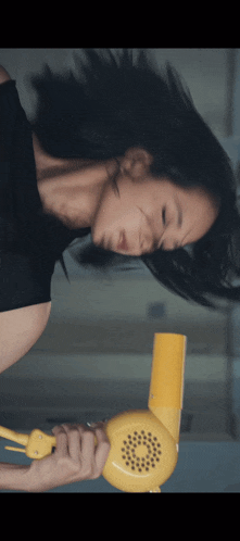 a woman holds a yellow hair dryer in her hand