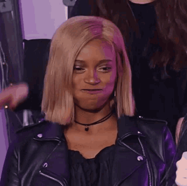 a woman wearing a black leather jacket and a choker makes a funny face