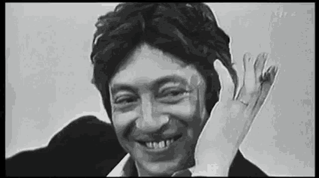 a black and white photo of a man smiling with his hand on his head