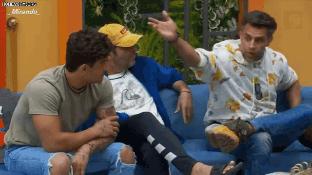 three men are sitting on a couch and one of them is wearing a hat that says coca cola