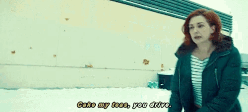 a woman in a green jacket says " cake my toes you drive " in front of a building