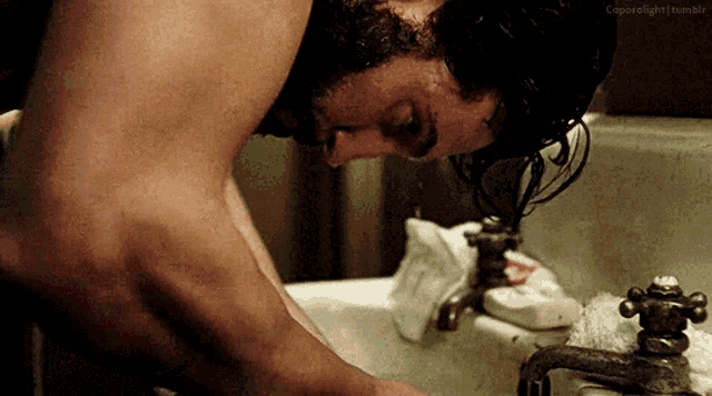 a shirtless man is washing his face in a bathroom sink with a caption that says coprolight tumblr