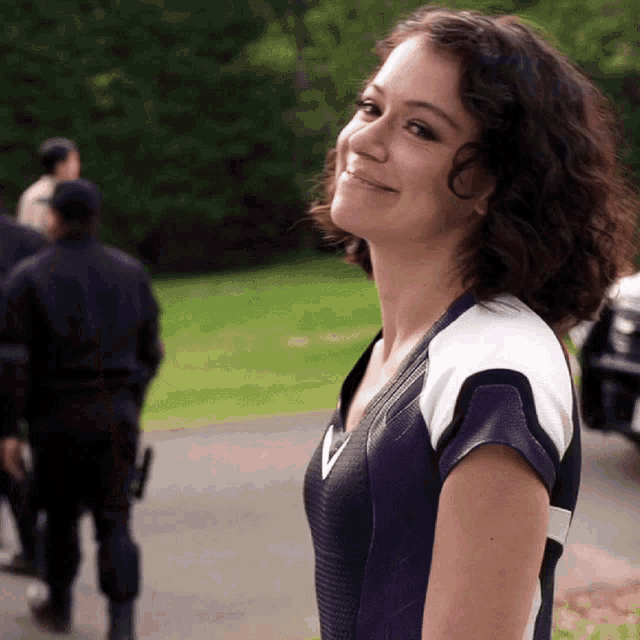 a woman in a purple and white top smiles in front of a group of people