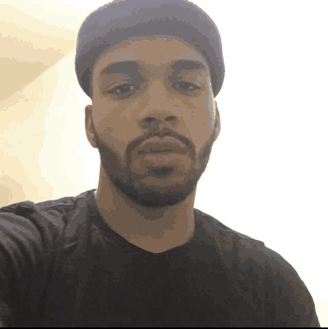 a man with a beard wears a black shirt and a black beanie