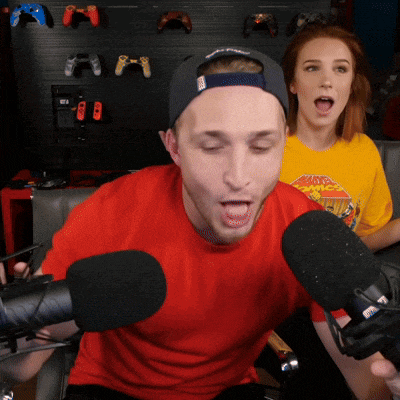 a man in a red shirt is speaking into a microphone while a woman in a yellow shirt looks on