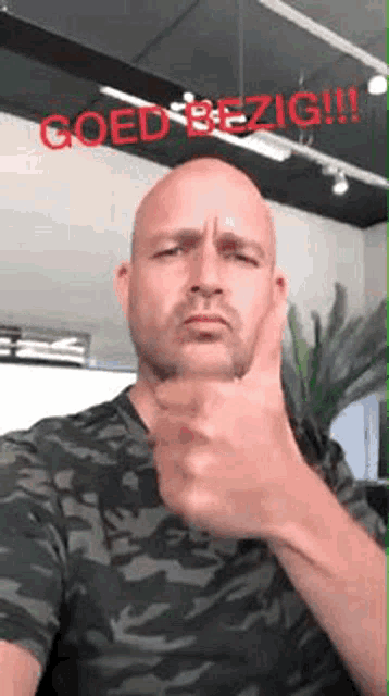 a bald man in a camo shirt is giving a thumbs up .
