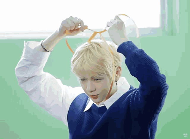 a young man with blonde hair is tying a ribbon around his head .
