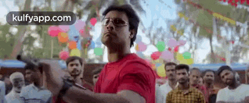a man in a red shirt and glasses is holding a gun in front of a crowd of people .