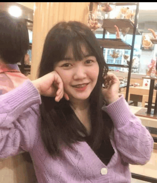a woman in a purple sweater is smiling with her hand on her forehead