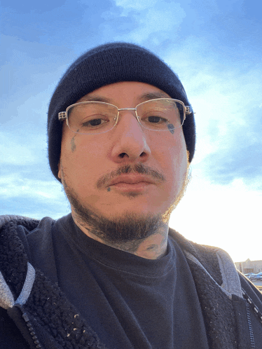 a man wearing glasses and a black beanie looks at the camera