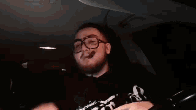a man with glasses is smoking a cigar while sitting in a car .