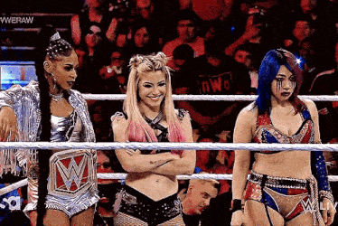 three women are standing in a wrestling ring with their arms crossed and smiling .