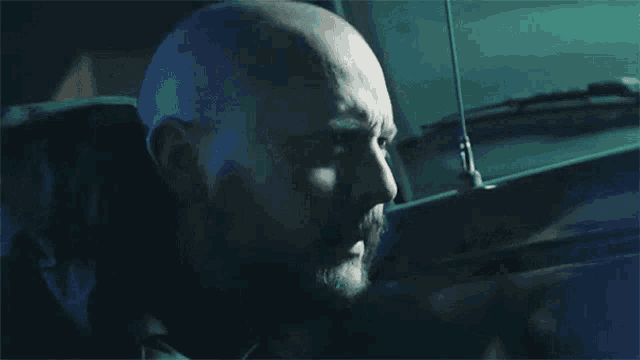 a bald man with a beard is sitting in a dark room