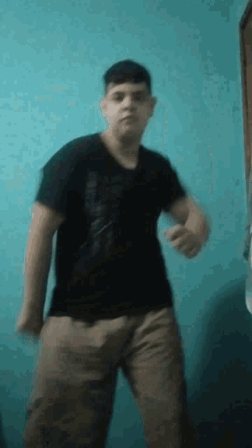 a man in a black shirt and khaki pants is standing in front of a blue wall
