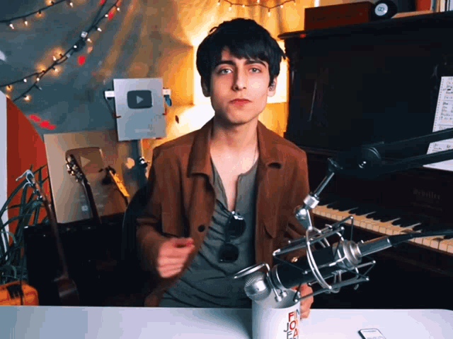 a young man in a brown jacket is standing in front of a microphone holding a cup that says flour on it