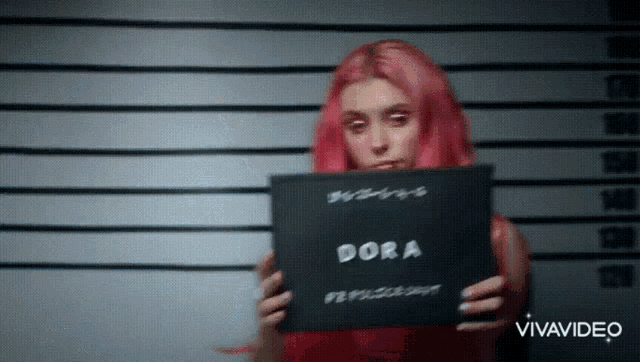 a woman with pink hair is holding up a photo of herself with the name dora on it