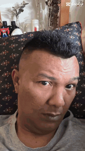 a man with a mohawk sits in front of a pillow that says capcut on it