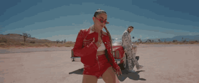 a man and a woman standing next to a red car in the desert
