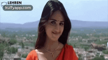 the woman is wearing a red saree and a necklace and smiling .