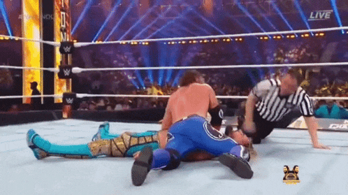 a wrestler is laying on the ground in a wrestling ring while a referee looks on .