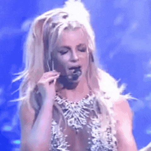a woman is singing into a microphone on a stage while wearing a necklace and earrings .