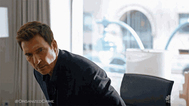 a man in a suit sits at a desk with the hashtag organizedcrime on the bottom