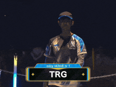 a man wearing a shirt that says trg stands in the dark