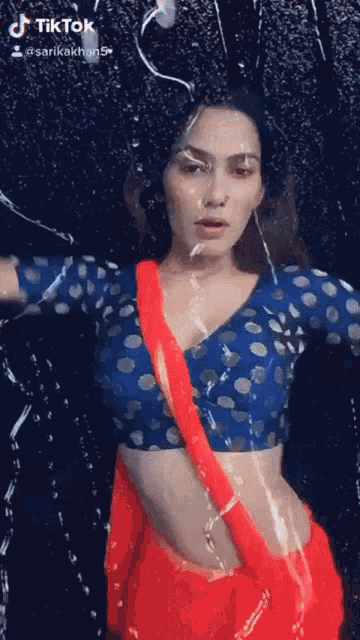 a woman in a red saree and blue polka dot blouse is dancing in the rain