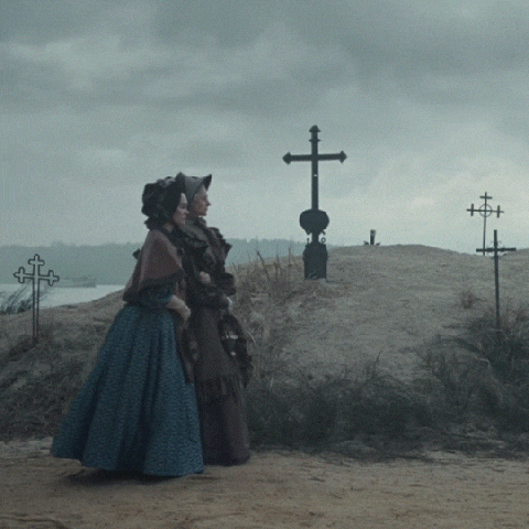 two women standing in front of a cemetery with a cross in the background