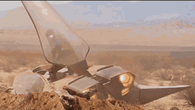 a man is riding a futuristic vehicle in the desert with mountains in the background