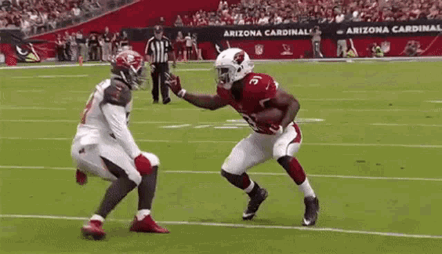 a football player from the arizona cardinals is running with the ball while another player tries to stop him .