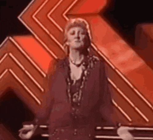 a woman in a purple dress is dancing on a stage in front of an orange background .