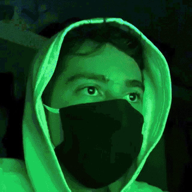 a man wearing a green hoodie and a black mask looks at the camera