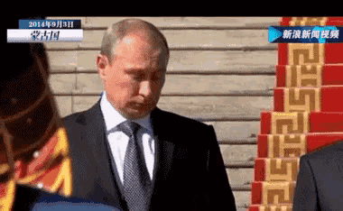 a man in a suit and tie is standing in front of a staircase with a greek key pattern on it