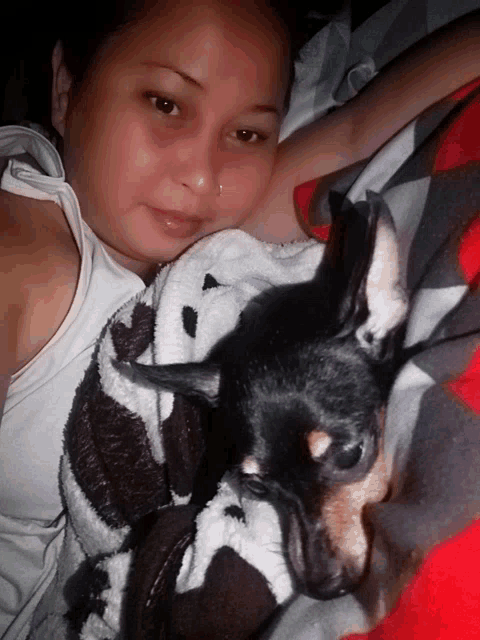 a woman is laying on a bed with a small black dog on her lap